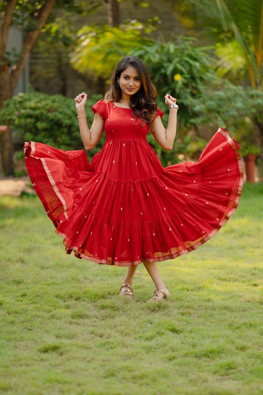 Red maxi dress with flowing tiered silhouette, elegant gold accents, and stylish casual party wear look in a garden setting.
